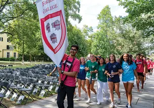Students marching; one at the front carries a red-and-white "Forbes College" banner.