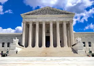 Front view of the U.S. Supreme Court building which is white stone and a staircase leading up to the eight pillars.