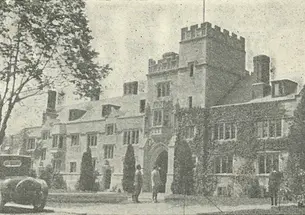 Black and white photo of a Gothic campus building, with an old-fashioned car parked in front.