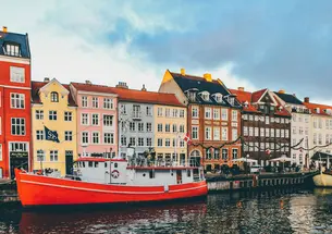 Row of colorful houses behind a a red boat behind a body of water. 