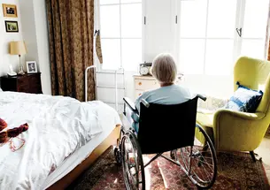An wheelchair bounc elderly womans sits alone in her room looking out the window