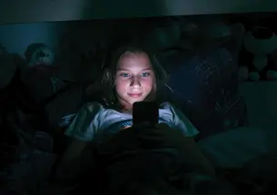 Young tween in bed in dark room on her phone