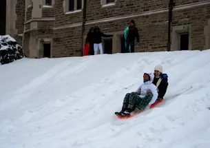 Two people ride a sled together down a snowy hill by Blair Arch.