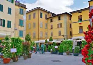 Yellow and pale white buildings surround a plaza with small trees and shrubs in Pistoia