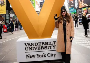 Stephanie Burset stands next to a giant V for Vanderbilt University in what looks like Times Square.