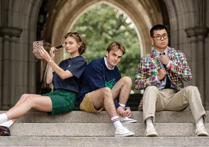 Three students sit on steps outside, with a pointed arch in the background.