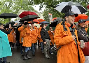People wearing orange rain jackets hold umbrellas and march in the 2026 P-rade.