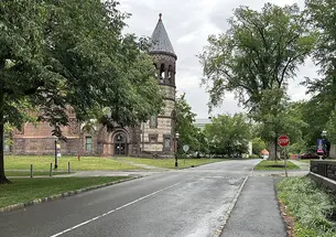 A road crossing with a Gothic building that has a turret in the background.