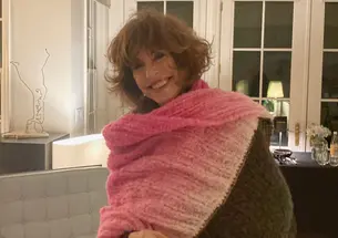Photo of Katherine Nouri Hughes smiling with short brown chin-length hair and wearing a pink scarf.