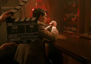 A man sits at a bar in red lighting; a director's clapboard is held in front.