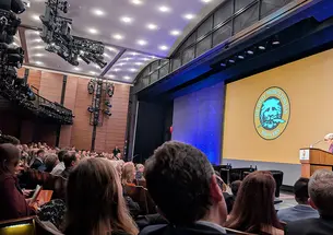 An auditorium full of attendees listen to a speaker standing in front of the Daily Princetonian's logo.