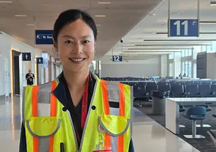 Janice Lee wears a yellow construction vest in an airport hallway, and there's a waiting area in the background.