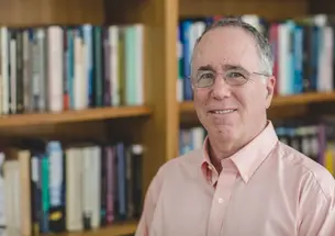 This is a shoulders-and-up photo of Gene M. Grossman with a bookcase in the background.