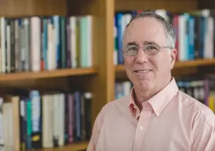 This is a shoulders-and-up photo of Gene M. Grossman with a bookcase in the background.