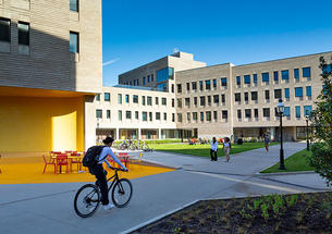 Student riding a bicycle next to dormitories