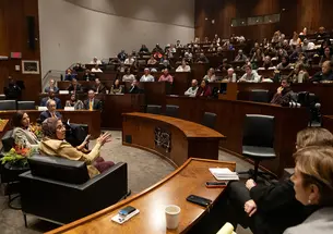 Three speakers seated in chairs at the front of a full lecture hall