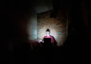 Frank Langfitt ’86 works in a bomb shelter in central Ukraine, the light from his laptop illuminating him and the brick wall behind him.