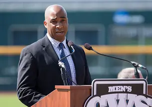 Damani Leech ’98 speaks at a podium with a baseball field in the background.