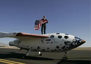 AITN_BrianBinnie.jpg Brian Binnie *78 stands on what looks like a small airplane, holding an American flag.