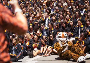 The Class of 2017 gathers in their black jackets behind the Tiger mascot, who's sitting on the ground and clapping his paws.