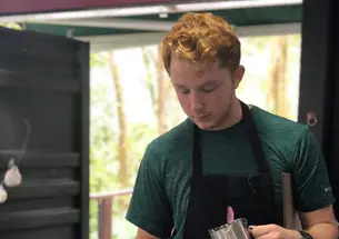 Alex Kaplan ’21 wears a black apron and holds a stainless steel container as he pours coffee into teacups.