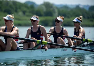 Four rowers at rest in a rowing shell on the water. Claire Collins is at left.