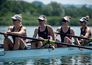 Four rowers at rest in a rowing shell on the water. Claire Collins is at left.