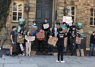 Students with Divest Princeton hold signs in front of Nassau Hall, made of cardboard and showing their support for Princeton divesting from fossil fuels.