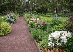 A path covered in reddish gravel leads past flowers to a wood bench.