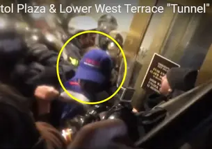 Someone with a blue baseball cap is seen near doors; people in riot gear are in the background.