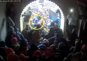 The view out of a crowded Capitol entrance tunnel; a yellow circle highlights Giberson facing the entrance wearing a blue baseball cap and a gaiter over his face.