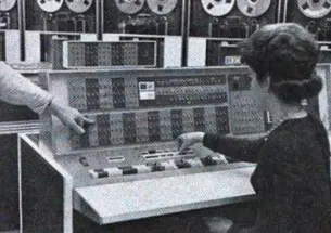 A woman sits at the controls of the room-sized IBM 7090 at Princeton’s Computer Center, manually entering instructions. You can see the data storage tapes at the top of the screen.