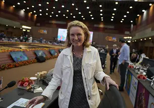 Isobel Coleman ’87 faces the camera and smiles in a room where each seat has a small screen. Blurry in the background are lit-up signs reading G20.