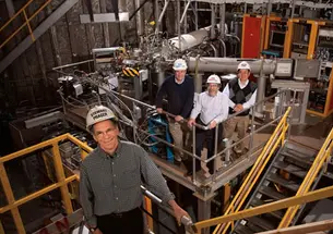 Stewart Prager, foreground, and from left, Richard Hawryluk, Robert Goldston *77, and Masayuki Ono *78 stand in front of the NSTX fusion machine, which is hidden by hardware.