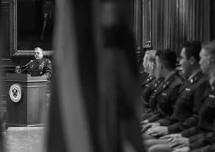 In this black and white photo, Gen. Mark Milley speaks at a podium on the left bearing the Princeton seal, while young men in military uniforms watch him from the right. 