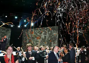 People at a party stand under a shower of confetti and streamers.