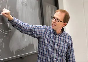 Andrew Houck draws on a blackboard with white chalk.