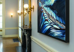 This is a photo "Pools," an abstract painting with lots of blue, hanging in Prospect House on a gray wall with a chair rail and crown moulding, next to a fireplace with a gilded mirror over it.