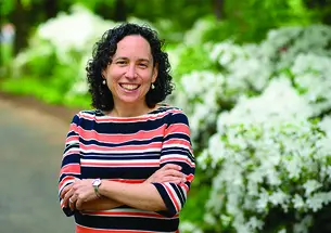 This is a photo of Rabbi Julie Roth outdoors, with green shrubs in the background.