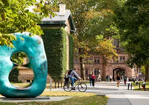 This is a photo of the Oval With Points sculpture with East Pyne and lots of students in the background.