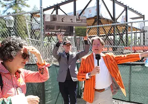 PAW-Art Museum tour001.jpg A man in an orange striped blazer speaks into a microphone in front of a construction site.