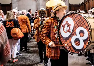 This is a photo of a few Princeton musicians wearing plaid blazers and straw hats while marching. The one in front has "08" printed on his drum.