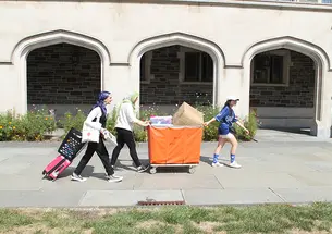 Three women push and pull a large orange bin.