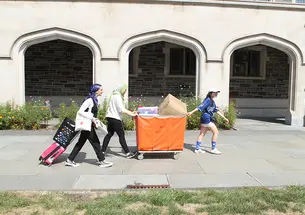 Three women push and pull a large orange bin.