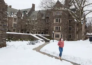 A masked student walks across campus, on a path cut through the snow, in 2021.