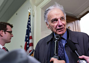 Ralph Nader speaks into a microphone to the press.