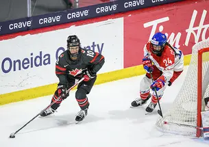 Two hockey players skate around the back of the goal.