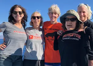Five women standing on a boat wear various Princeton T-shirts.