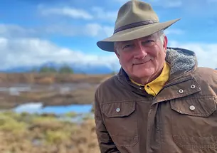 This is a photo of Bill Urschel ’78 with blue sky and an Alaskan summer landscape in the background.