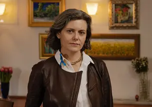 This is a photo of Dora Chomiak ’91 in front of a wall hung with paintings.